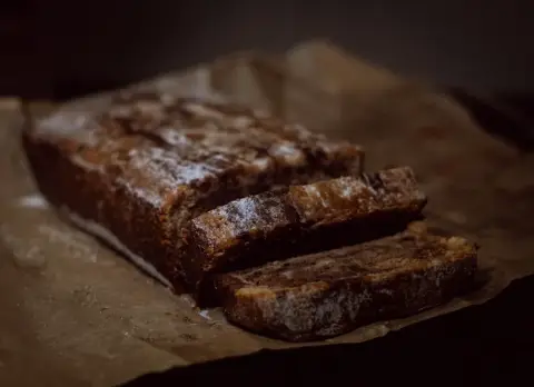 A dark sticky ginger loaf, partly sliced, on baking parchment