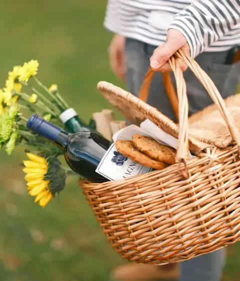 A wicker hamper carried through the orchard, packed with bread and wine