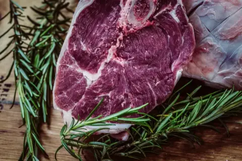 A bone-in lamb shoulder with sprigs of rosemary on the counter
